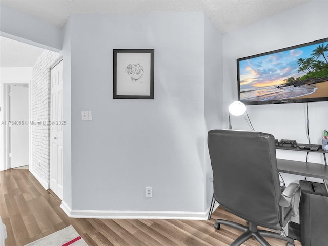 office space featuring brick wall, hardwood / wood-style floors, and a textured ceiling