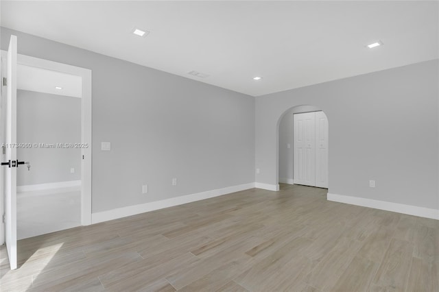 unfurnished room featuring arched walkways, visible vents, light wood-style flooring, and baseboards