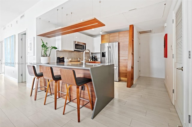 kitchen with appliances with stainless steel finishes, white cabinetry, backsplash, a kitchen bar, and kitchen peninsula