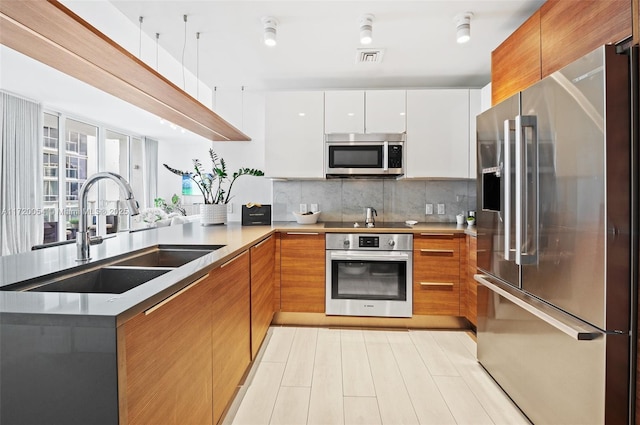 kitchen with appliances with stainless steel finishes, white cabinetry, sink, backsplash, and kitchen peninsula