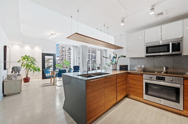 kitchen featuring appliances with stainless steel finishes, white cabinetry, sink, backsplash, and light hardwood / wood-style flooring