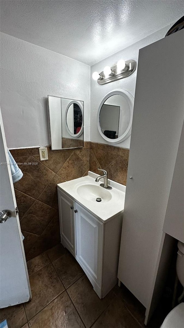 bathroom with tile walls, tile patterned flooring, vanity, a textured ceiling, and toilet