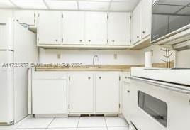 kitchen with white cabinets, light tile patterned floors, a drop ceiling, and stove