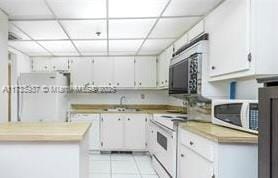 kitchen featuring a paneled ceiling, sink, white cabinets, light tile patterned floors, and white appliances