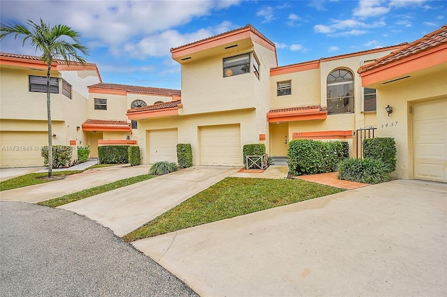 townhome / multi-family property featuring a garage, a tile roof, driveway, and stucco siding