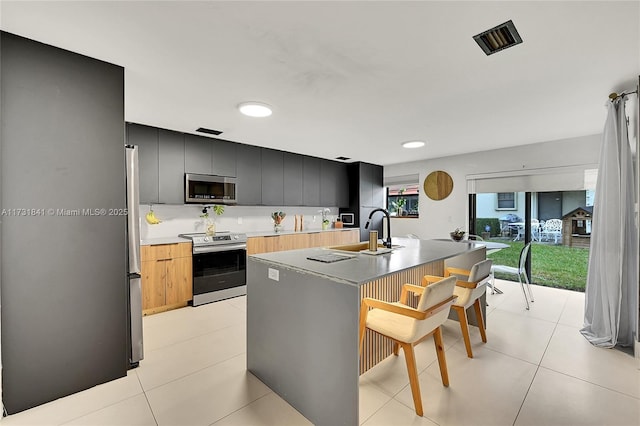 kitchen featuring light tile patterned flooring, appliances with stainless steel finishes, sink, and a center island with sink