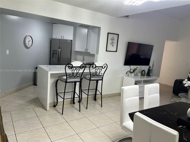 kitchen with white cabinetry, a kitchen breakfast bar, light tile patterned floors, stainless steel refrigerator with ice dispenser, and a textured ceiling