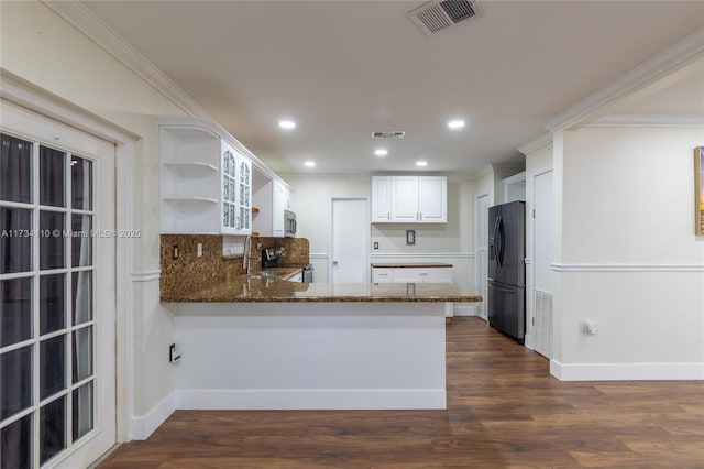 kitchen with dark wood-type flooring, dark stone countertops, white cabinets, black fridge, and kitchen peninsula