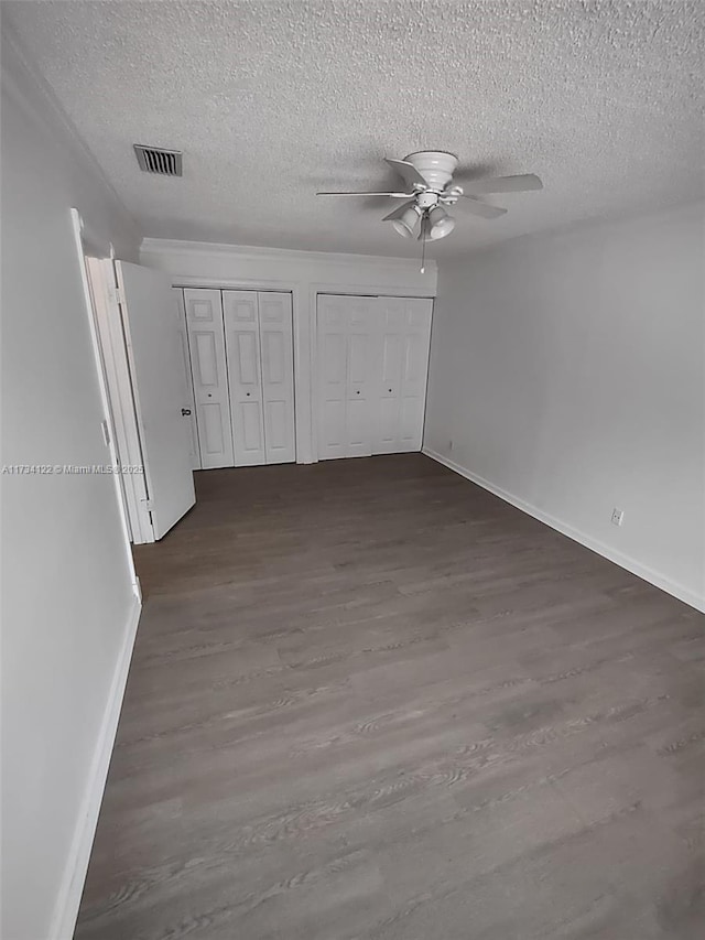 unfurnished bedroom featuring multiple closets, a textured ceiling, dark hardwood / wood-style floors, and ceiling fan