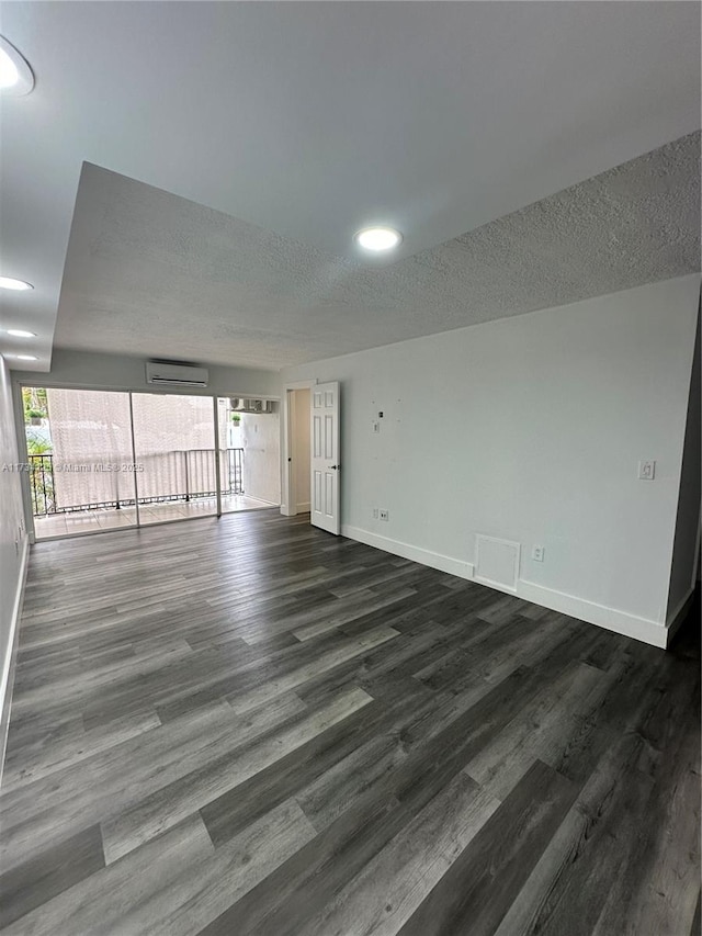 unfurnished room featuring dark wood-type flooring, a wall mounted AC, and a textured ceiling