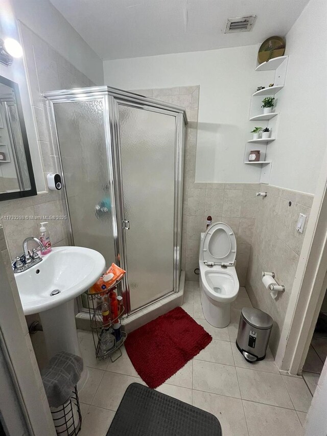 bathroom featuring tile patterned floors, toilet, a shower with door, and tile walls