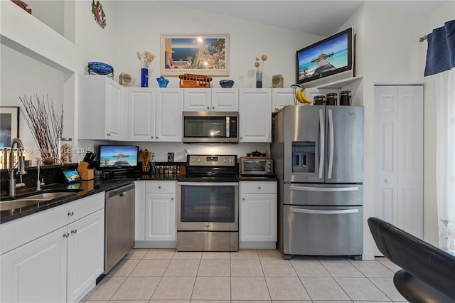 kitchen with sink, light tile patterned floors, white cabinetry, stainless steel appliances, and vaulted ceiling