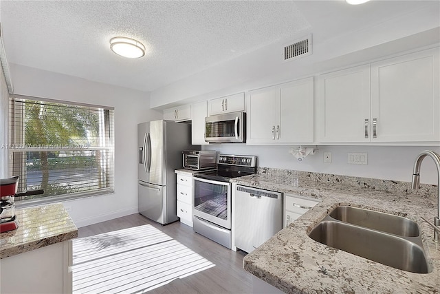 kitchen featuring sink, appliances with stainless steel finishes, light stone countertops, a textured ceiling, and white cabinets