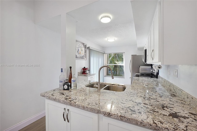 kitchen featuring sink, light stone counters, a textured ceiling, appliances with stainless steel finishes, and white cabinets