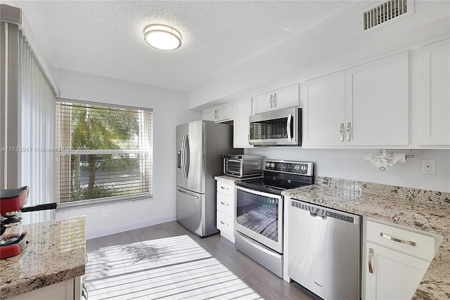 kitchen featuring appliances with stainless steel finishes, white cabinetry, dark hardwood / wood-style flooring, light stone counters, and a textured ceiling