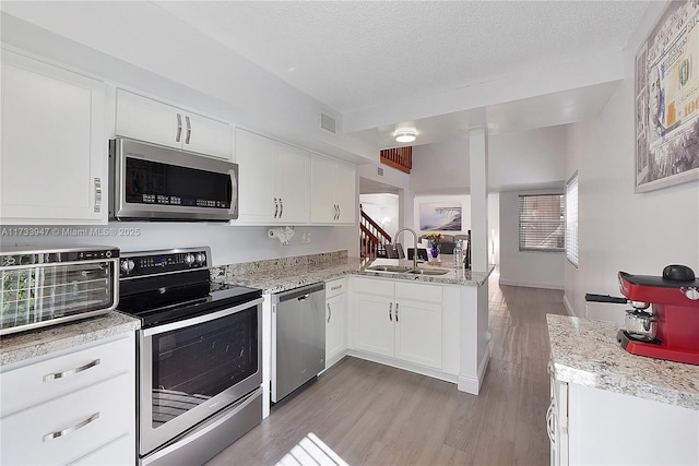 kitchen with appliances with stainless steel finishes, sink, white cabinets, kitchen peninsula, and a textured ceiling