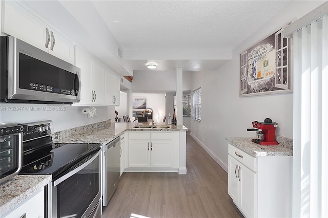 kitchen with white cabinetry, sink, kitchen peninsula, stainless steel appliances, and light wood-type flooring