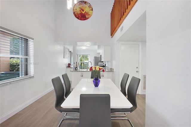 dining room featuring sink, light hardwood / wood-style flooring, and a high ceiling