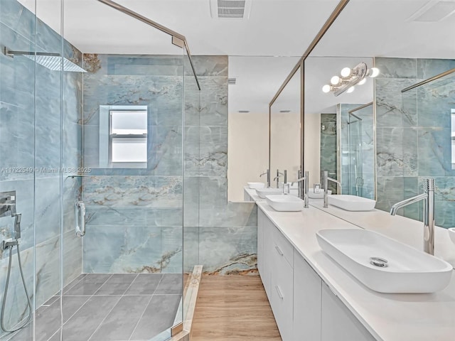 bathroom featuring a shower with door, vanity, and tile walls