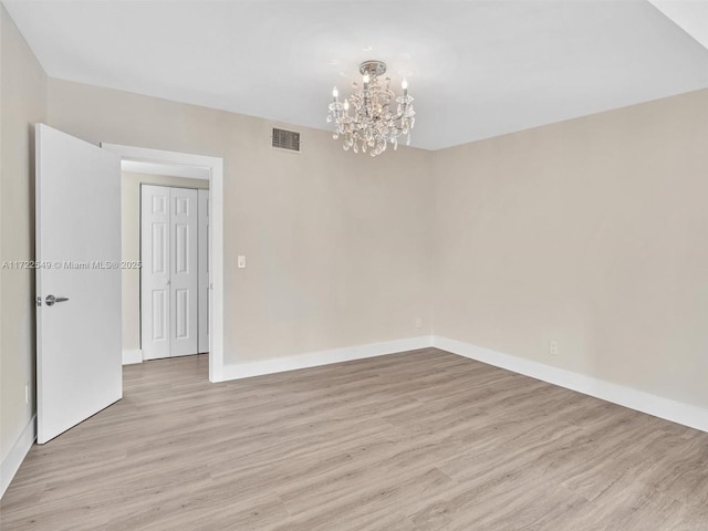 spare room featuring a notable chandelier and light wood-type flooring