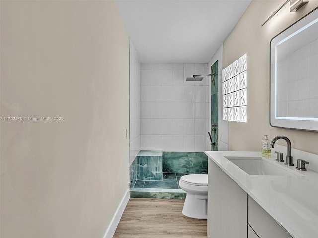 bathroom with a tile shower, vanity, wood-type flooring, and toilet