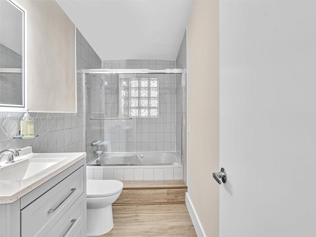 full bathroom featuring combined bath / shower with glass door, tile walls, hardwood / wood-style floors, vanity, and toilet