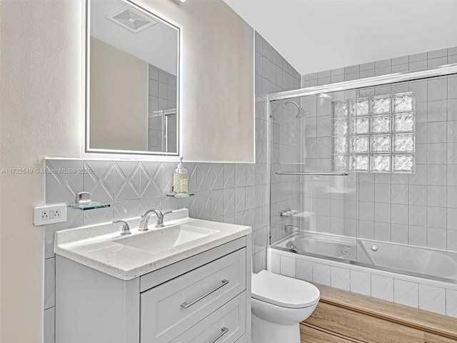 full bathroom with vanity, tile walls, shower / bath combination with glass door, and toilet