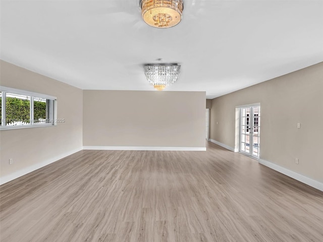 spare room featuring an inviting chandelier, a wealth of natural light, light hardwood / wood-style floors, and french doors