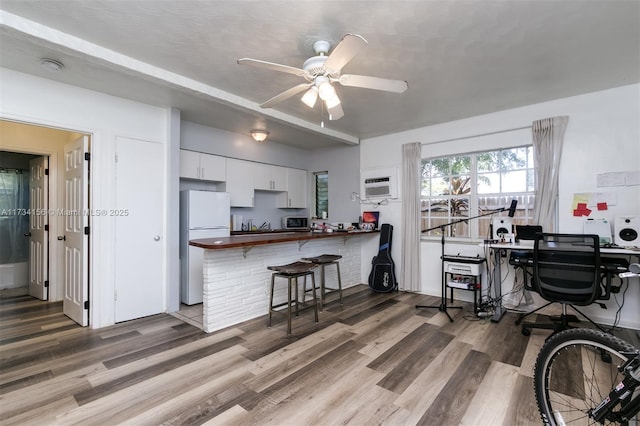 kitchen featuring a breakfast bar area, white cabinetry, wood-type flooring, white refrigerator, and kitchen peninsula