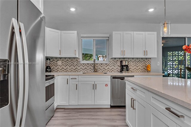 kitchen featuring stainless steel appliances, light stone countertops, decorative backsplash, and white cabinets