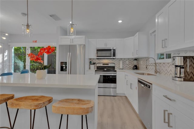 kitchen featuring white cabinetry, appliances with stainless steel finishes, decorative light fixtures, and sink