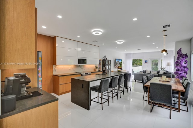 kitchen with sink, a breakfast bar area, white cabinetry, hanging light fixtures, and decorative backsplash