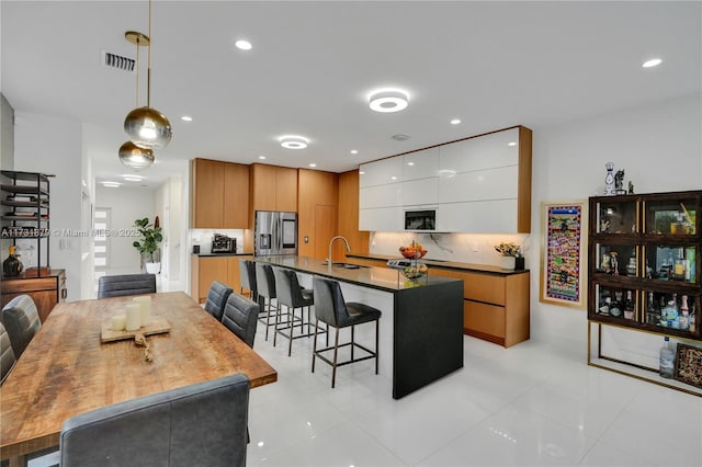 kitchen with stainless steel refrigerator with ice dispenser, a kitchen bar, sink, white cabinetry, and pendant lighting