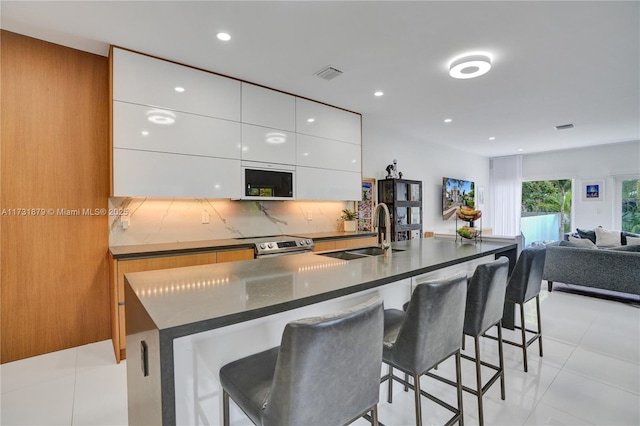 kitchen featuring sink, backsplash, white cabinets, a kitchen breakfast bar, and a center island with sink