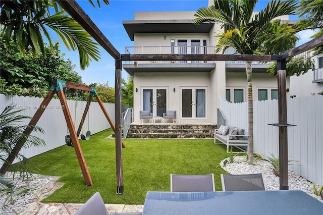 back of property with french doors, a balcony, a yard, and a playground