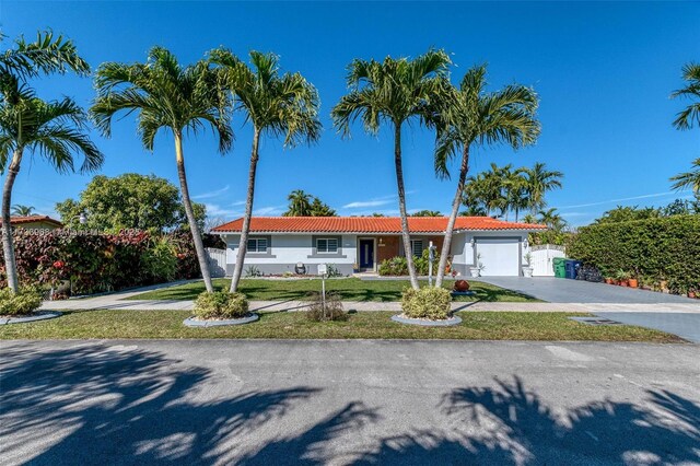 single story home featuring a tiled roof, driveway, a garage, a front lawn, and stucco siding
