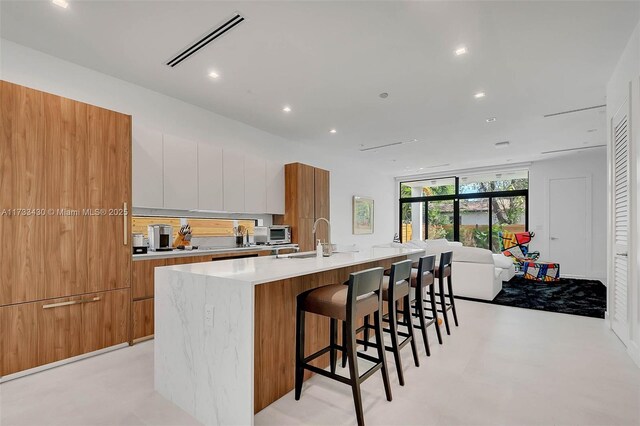 kitchen with white cabinetry, a kitchen bar, sink, and a large island with sink