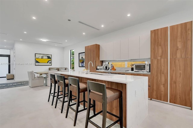 kitchen with modern cabinets, a breakfast bar, light countertops, and an island with sink