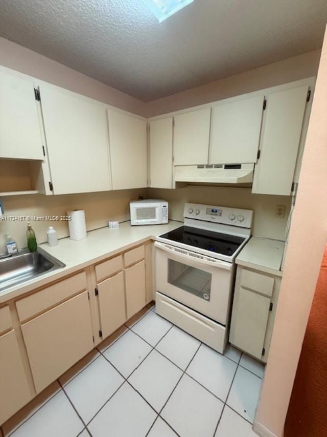 kitchen with light tile patterned flooring, sink, white appliances, a textured ceiling, and cream cabinetry