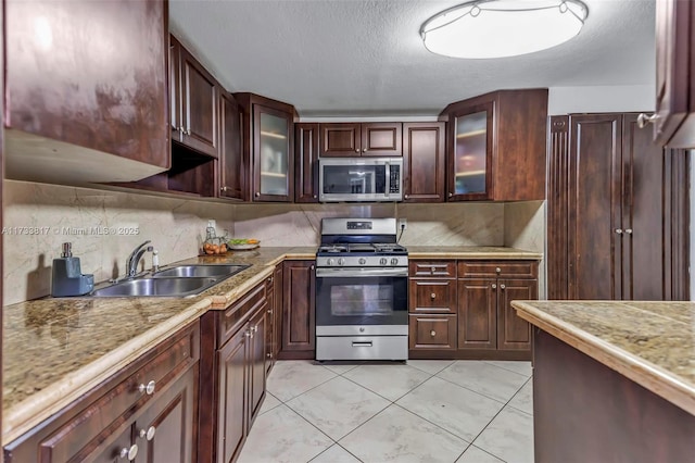 kitchen featuring tasteful backsplash, sink, light tile patterned floors, stainless steel appliances, and a textured ceiling