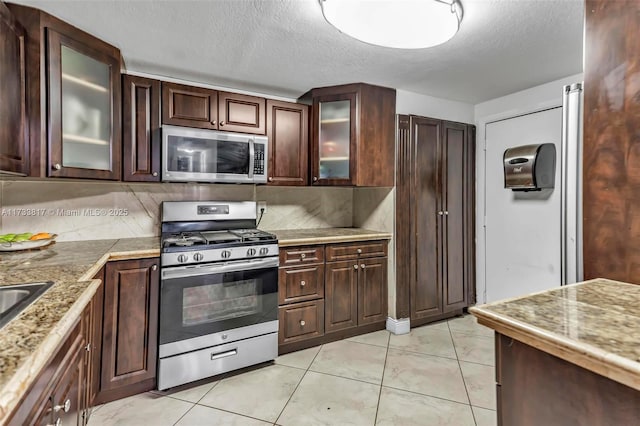 kitchen featuring tasteful backsplash, light tile patterned floors, stainless steel appliances, and a textured ceiling