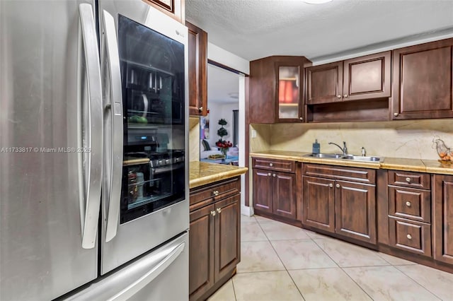 kitchen featuring light tile patterned flooring, stainless steel refrigerator, tasteful backsplash, sink, and a textured ceiling