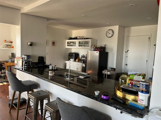 kitchen with stainless steel refrigerator, a kitchen bar, kitchen peninsula, and hardwood / wood-style flooring