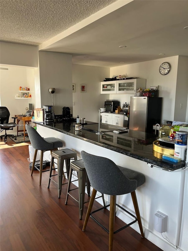 kitchen with dark wood-type flooring, a textured ceiling, stainless steel refrigerator, a kitchen breakfast bar, and kitchen peninsula