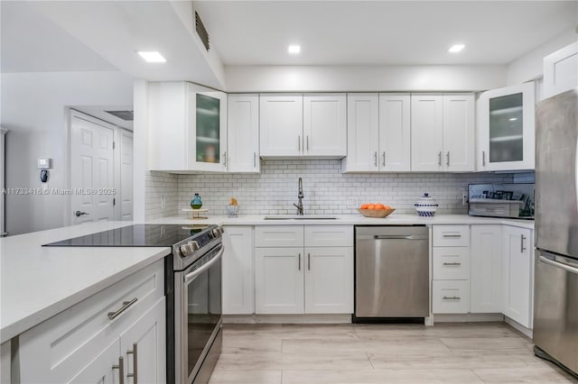 kitchen with tasteful backsplash, sink, white cabinets, light hardwood / wood-style floors, and stainless steel appliances