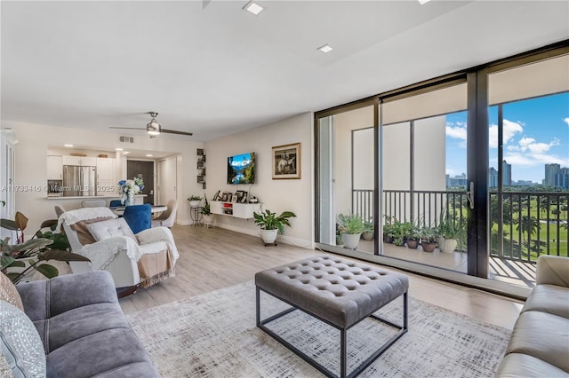 living room featuring ceiling fan, a wall of windows, and light hardwood / wood-style floors