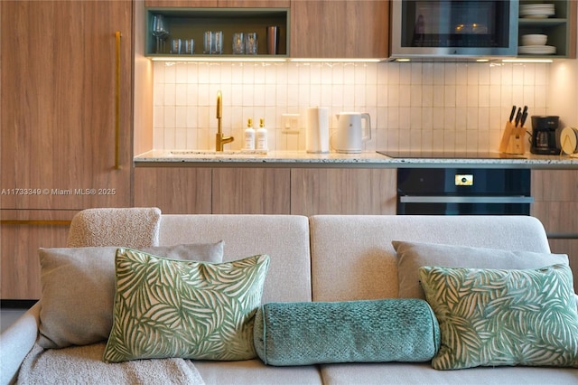 kitchen featuring light stone counters, backsplash, wall oven, and a sink