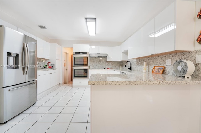 kitchen featuring light tile patterned flooring, white cabinetry, appliances with stainless steel finishes, kitchen peninsula, and backsplash