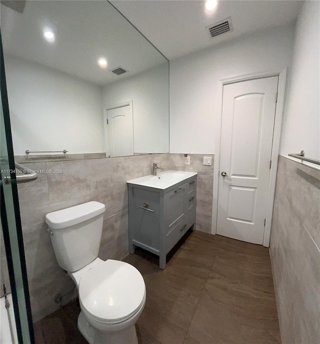 bathroom featuring tile patterned floors, vanity, toilet, and tile walls