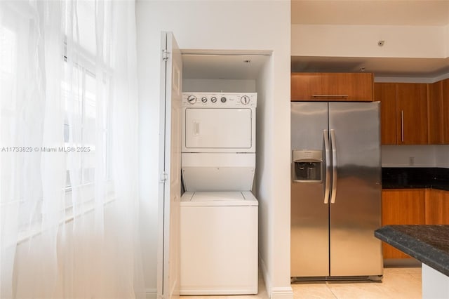 kitchen with stacked washer / drying machine, light tile patterned flooring, dark stone counters, and stainless steel refrigerator with ice dispenser